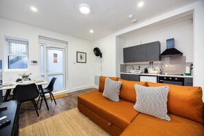 A compact living space with a sofa, dining table, chairs, and a kitchenette. - Earl`s Court Residence | Elegant 1BR | London (London)