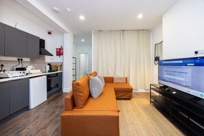 Una sala de estar moderna con un sofá, televisión y una cocina equipada con refrigerador y estufa.