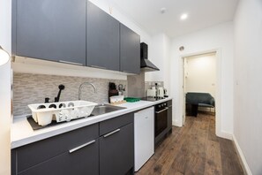 Cocina pequeña con armarios oscuros, una encimera blanca y un lavavajillas integrado.