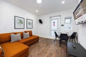 A modern living room with a sofa, a dining table with chairs, and framed artwork on the wall. - Earl`s Court Residence | Elegant 1BR | London (London)