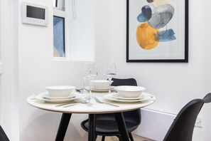 Un comedor con una mesa redonda dispuesta para cuatro personas, platos y cuencos blancos, cubiertos y copas de vino.