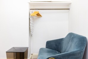 Una habitación con una silla azul, un perchero con un colgador amarillo y una cortina estampada.