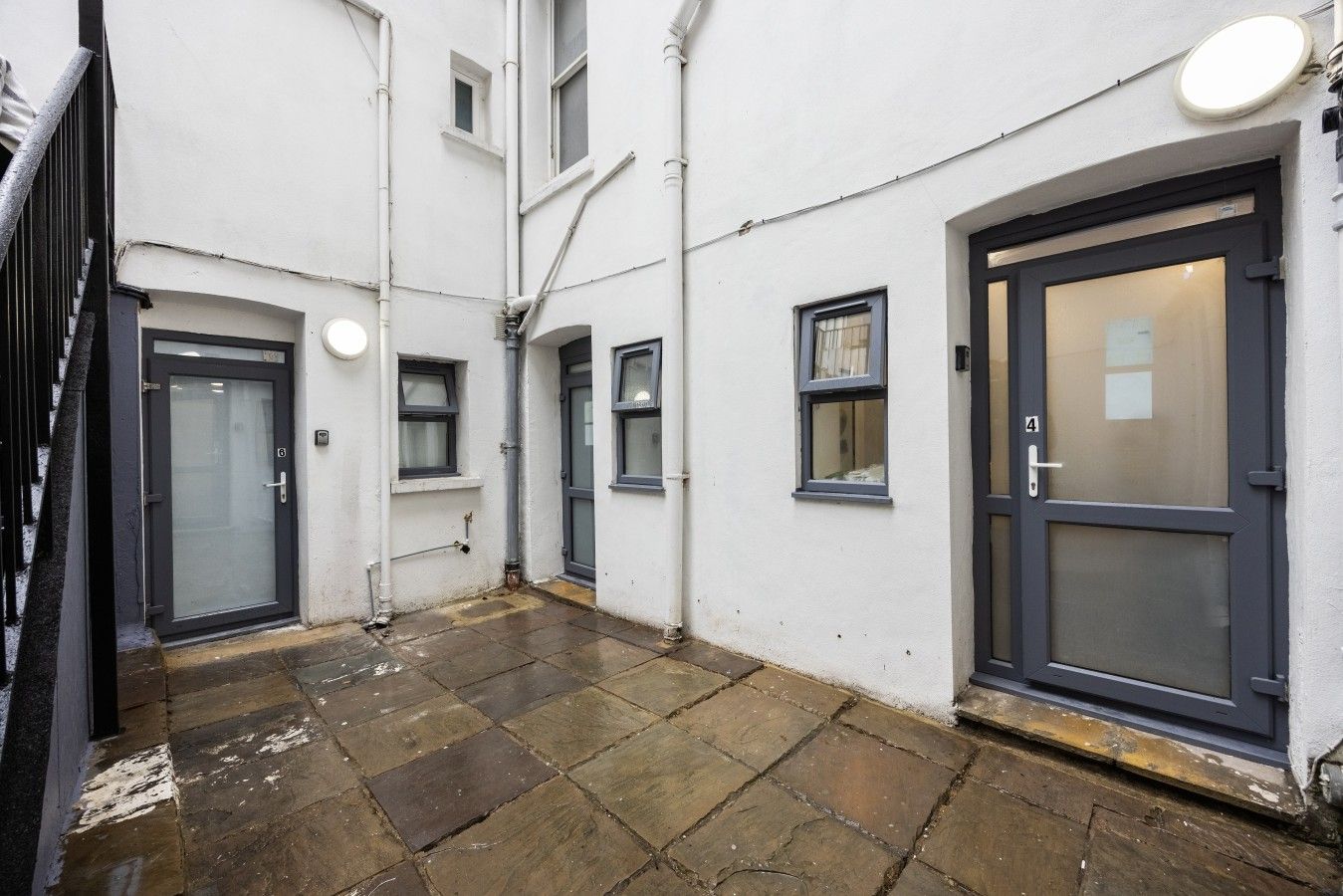 A narrow alleyway with a tiled floor, a door with a number plate, and a window with a curtain.