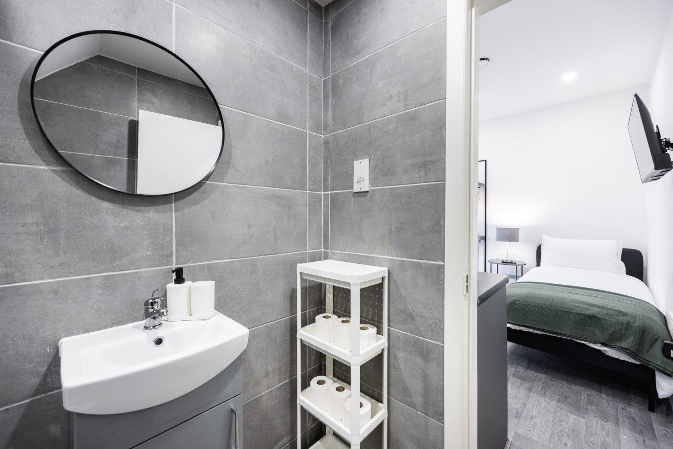 A modern bathroom with a round mirror, a white sink, and a toilet paper holder.