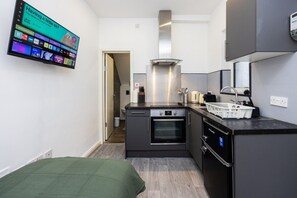 A compact kitchen with a built-in oven, a microwave, and a coffee maker. There is a small dining area with a bench and a green throw blanket. - Earl`s Court Residence | Elegant Studio | London (Greater London)