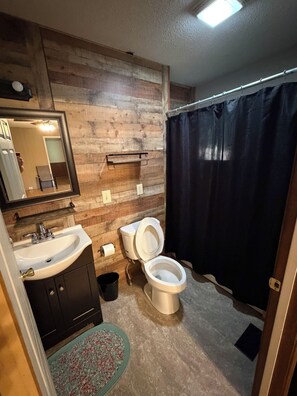 Une salle de bain avec un mur en bois, un lavabo, des toilettes et un rideau de douche.