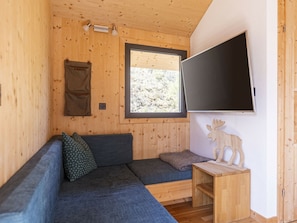 Ein gemütliches Blockhaus-Interieur mit einer Holzwand, einem großen Fenster, einem Flachbildfernseher, einer Couch und einem kleinen Holztisch.