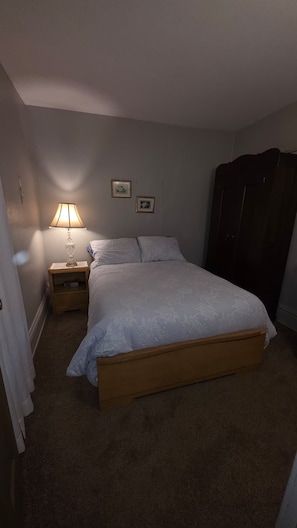 Un dormitorio con cama, mesita de noche, lámpara y armario.