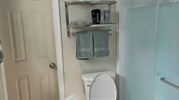 Une salle de bain comprenant des toilettes, un espace de douche vitré, un porte-serviettes avec des serviettes et une poubelle.