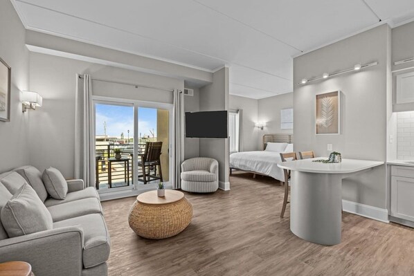A modern hotel room with a sofa, a round table, a bed, a TV, and a balcony with a view. - Waterfront Perch | King Suite · Steps to DT MHC (Morehead City)