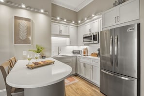 A modern kitchen with white cabinetry, stainless steel appliances, and a central island with a glass top. - Captains Quarters at Big Rock Landing| King Suite · Steps to DT MHC (Morehead City)