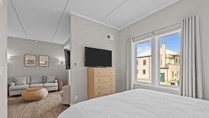 Habitación de hotel moderna con una cama grande, televisión, cómoda de madera, sofá y vistas a la ciudad.