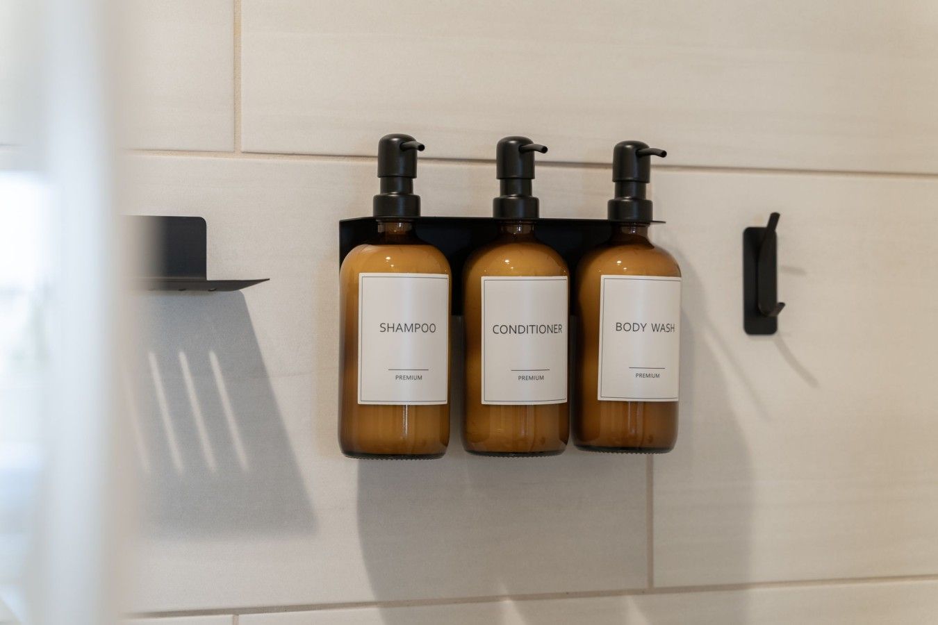Tres botellas de champú, acondicionador y gel de baño sujetas a una pared negra.