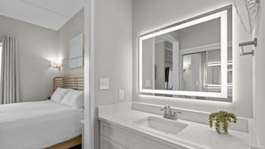 Una habitación de hotel con una cama, un espejo grande, un lavamanos blanco y una planta pequeña.