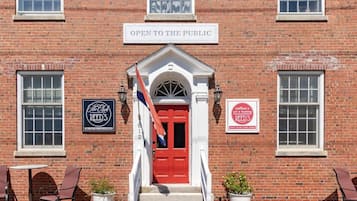 Un edificio de ladrillo con una puerta roja, un letrero que dice 'ABIERTO AL PÚBLICO' y dos carteles que anuncian 'The Club REED'S' y 'café + arte + enmarcación'.