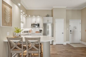 A modern kitchen with white cabinetry, stainless steel appliances, and a central island with two chairs. - Captains Quarters at Big Rock Landing| King Suite · Steps to DT MHC (Morehead City)