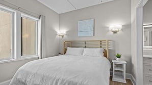 Un dormitorio con cama, mesitas de noche, una lámpara de pared y una ventana.