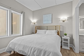 A bedroom with a bed, bedside tables, a nightstand, a wall-mounted light, and a window. - Waterfront Perch | King Suite · Steps to DT MHC (Morehead City)