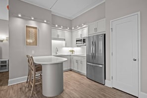 A modern kitchen with white cabinets, a stainless steel refrigerator, and a central island. - Waterfront Perch | King Suite · Steps to DT MHC (Morehead City)