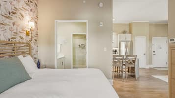 Una habitación de hotel con cama, baño con ducha, zona de comedor con mesa y sillas, y cocina.