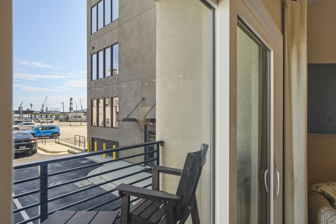 Een balkon met uitzicht op een parkeerplaats en een gebouw met grote ramen.