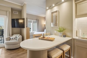 A modern living room with a dining area, a flat-screen TV mounted on the wall, a large window, and a view of the outdoors. - Captains Quarters at Big Rock Landing| King Suite · Steps to DT MHC (Morehead City)