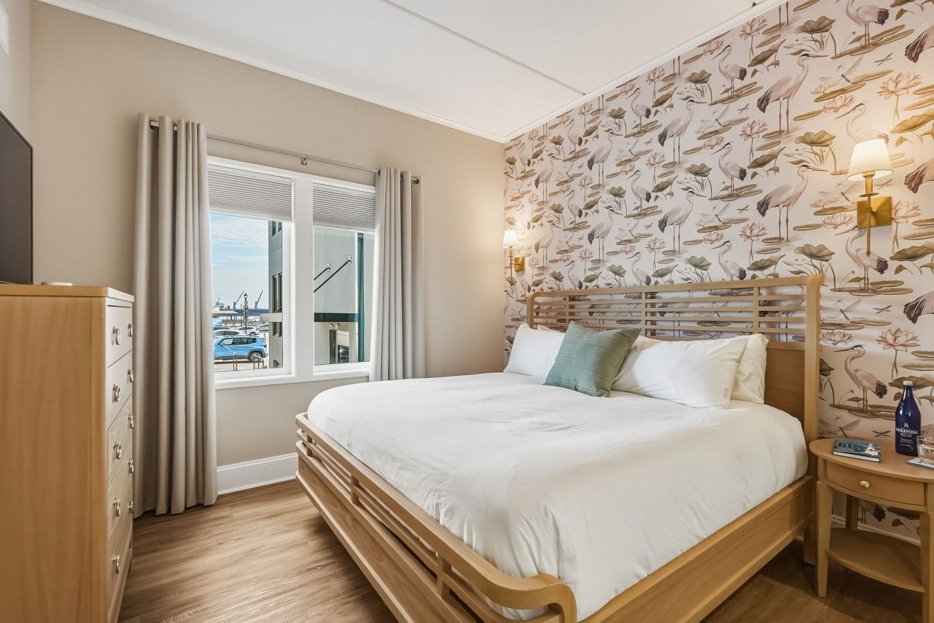 Habitación de hotel con cama, mesita de noche, lámpara, armario y ventana con cortinas.
