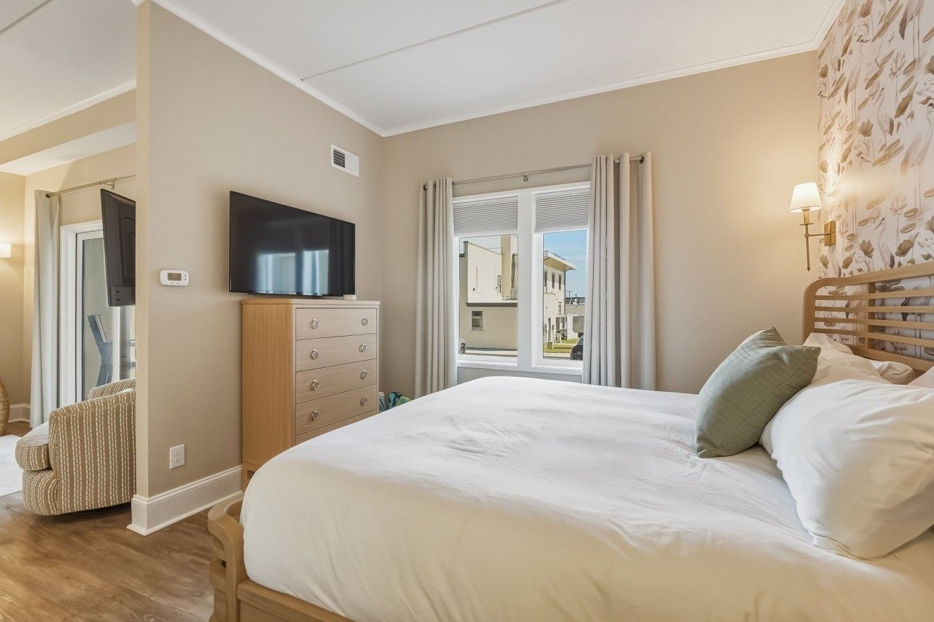 Un dormitorio con una cama, televisión, cómoda y ventana con cortinas.