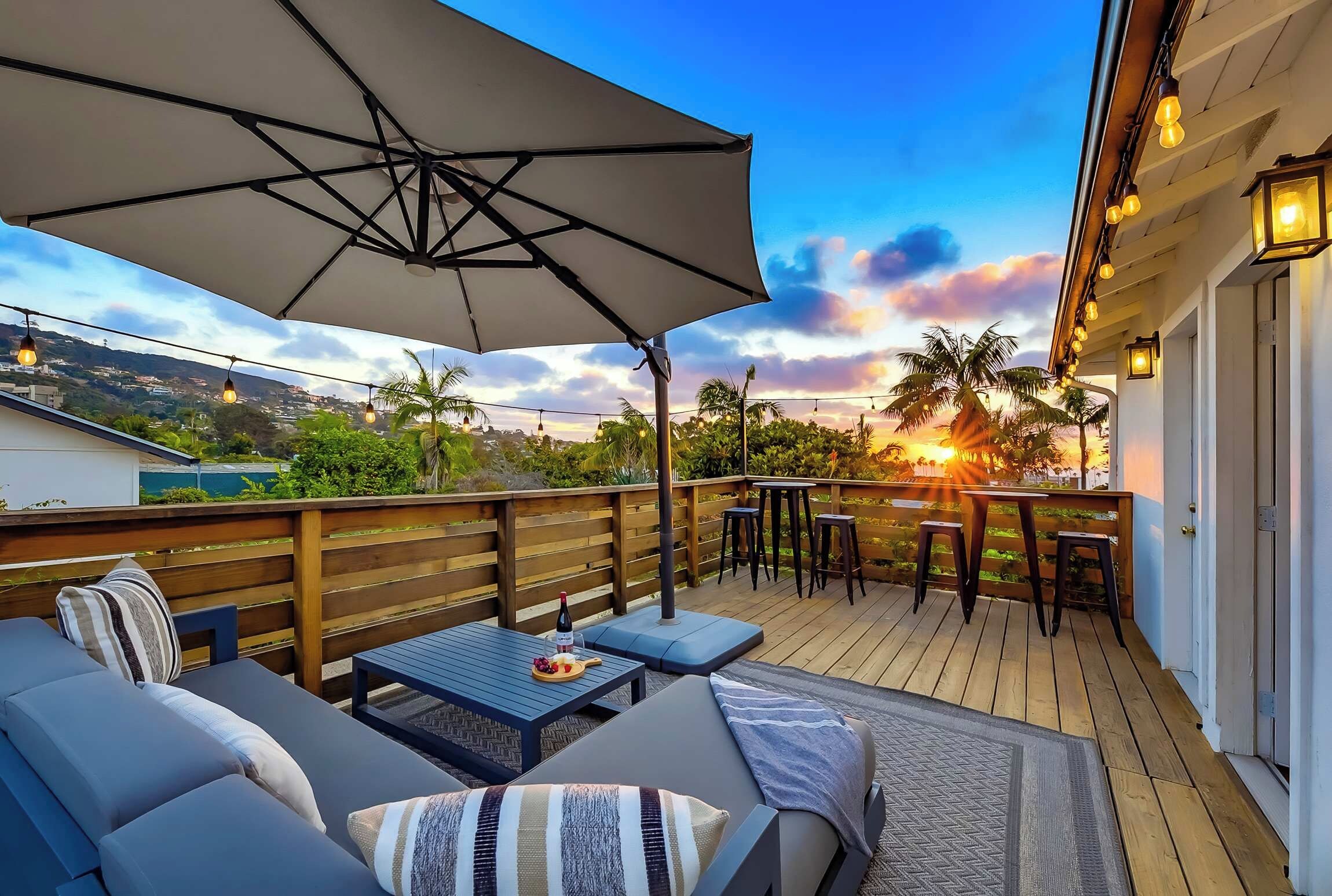 A deck with outdoor seating, a table with a bottle, and a view of the sunset.