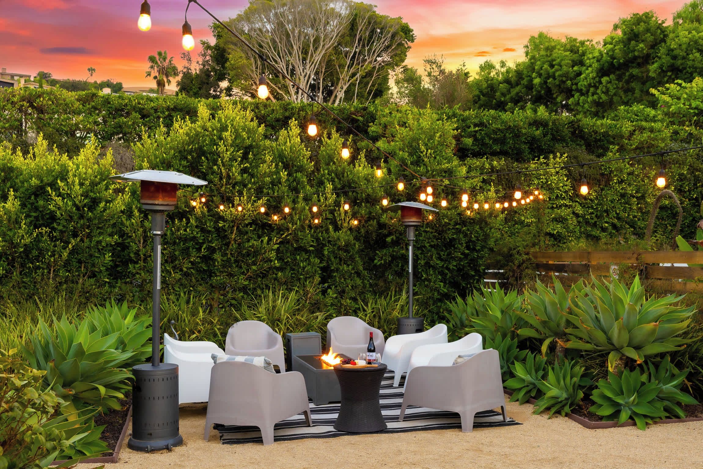 An outdoor seating area with chairs and a table, surrounded by greenery and string lights.