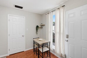 A small dining area with a table and chairs, a white door, and a window with curtains. -  Your cozy little getaway in Tampa! Enjoy a private studio in a perfect location (Tampa)