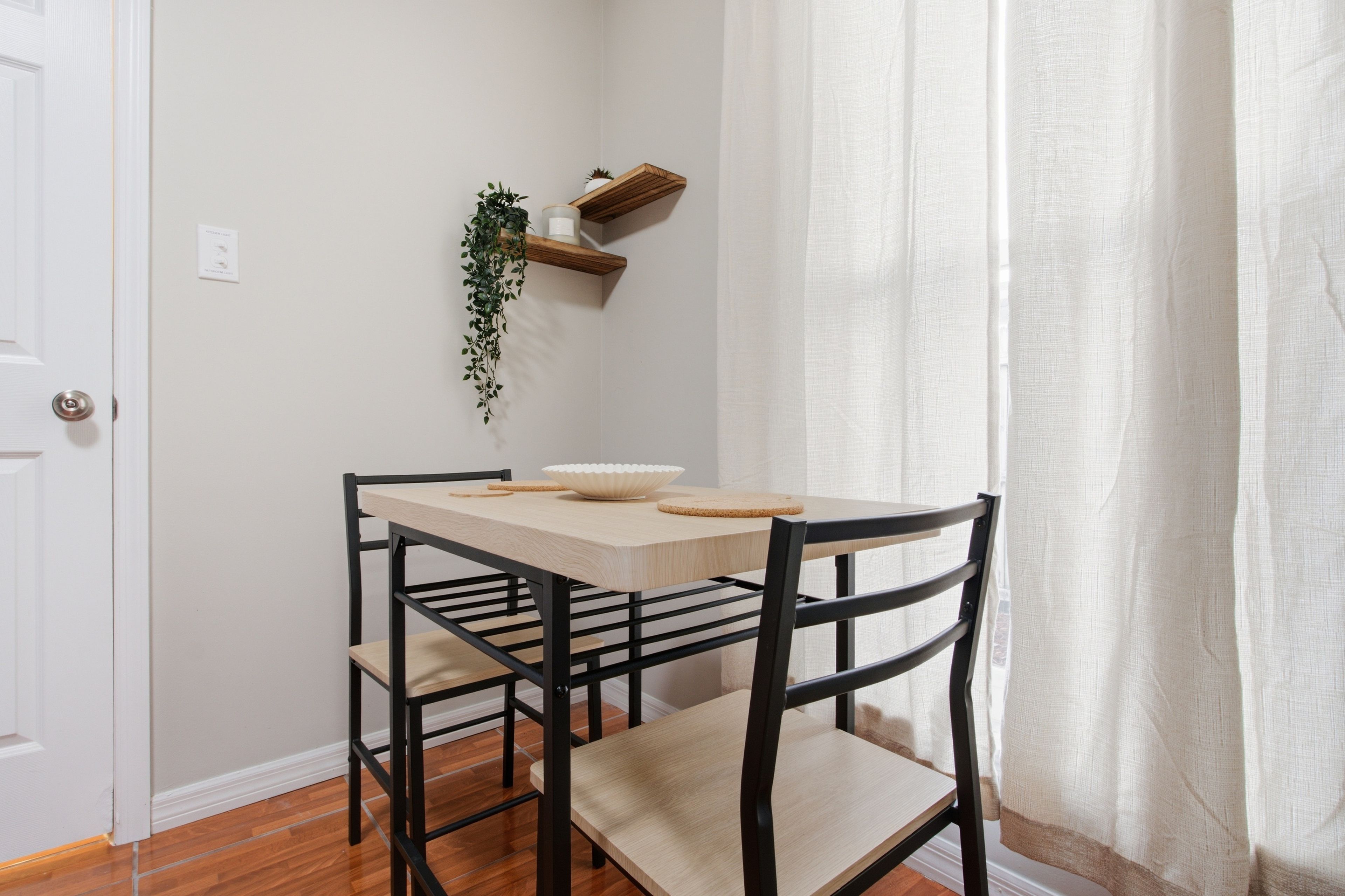 A dining area with a table and four chairs, a hanging plant, and a wooden shelf.