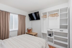 A bedroom with a bed, a TV mounted on the wall, a wardrobe with hangers, and a small table with a basket. -  Your cozy little getaway in Tampa! Enjoy a private studio in a perfect location (Tampa)
