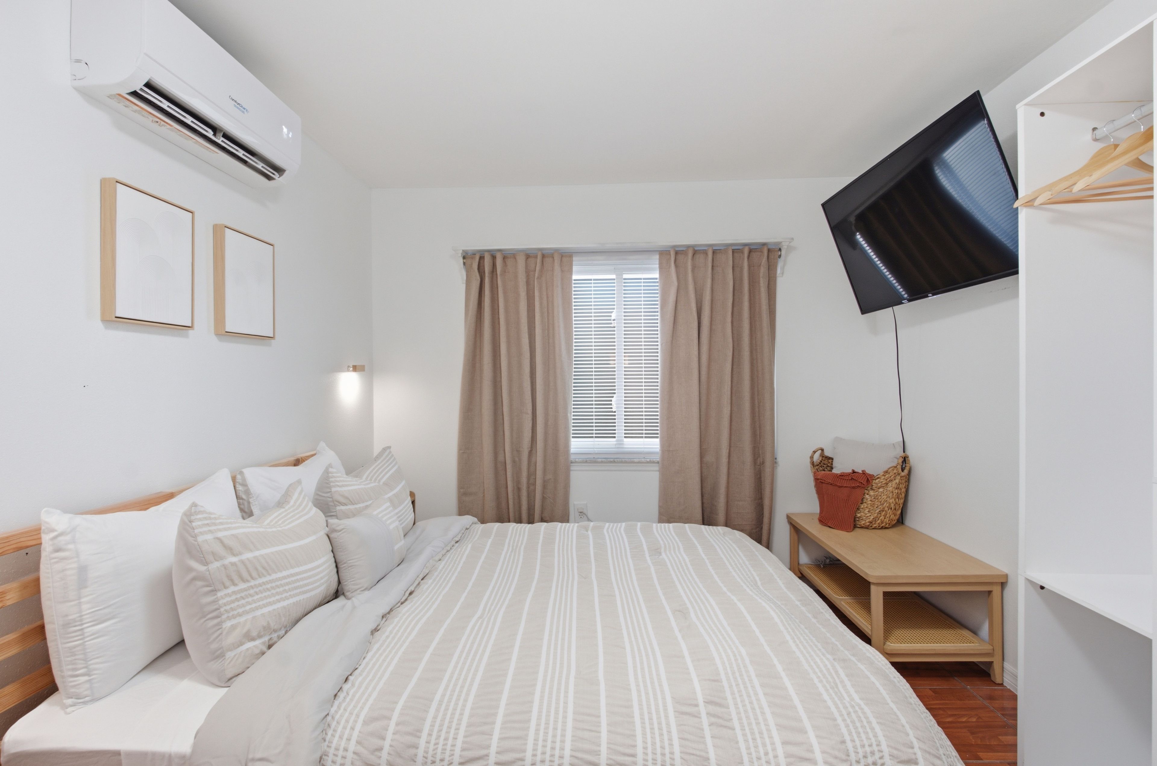 Une chambre d’hôtel avec un lit, un téléviseur fixé au mur, une fenêtre avec des rideaux et une table de chevet.