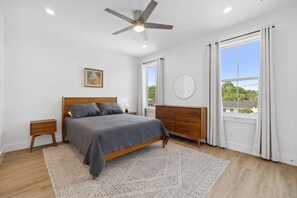 A bedroom with a bed, bedside tables, a dresser, a ceiling fan, a window with curtains, and a wall-mounted round mirror. - ☀️Blissful Getaway - Private Pool 🏊‍♀️- Patio 🌴 (Panama City)