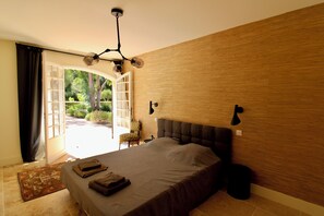 A bedroom with a bed, a chair, a lamp, and a view of the outdoors. - Villa Médicis – Sleeps 10, Private Pool, A/C & Walking Distance to the Sea (Le Pradet)