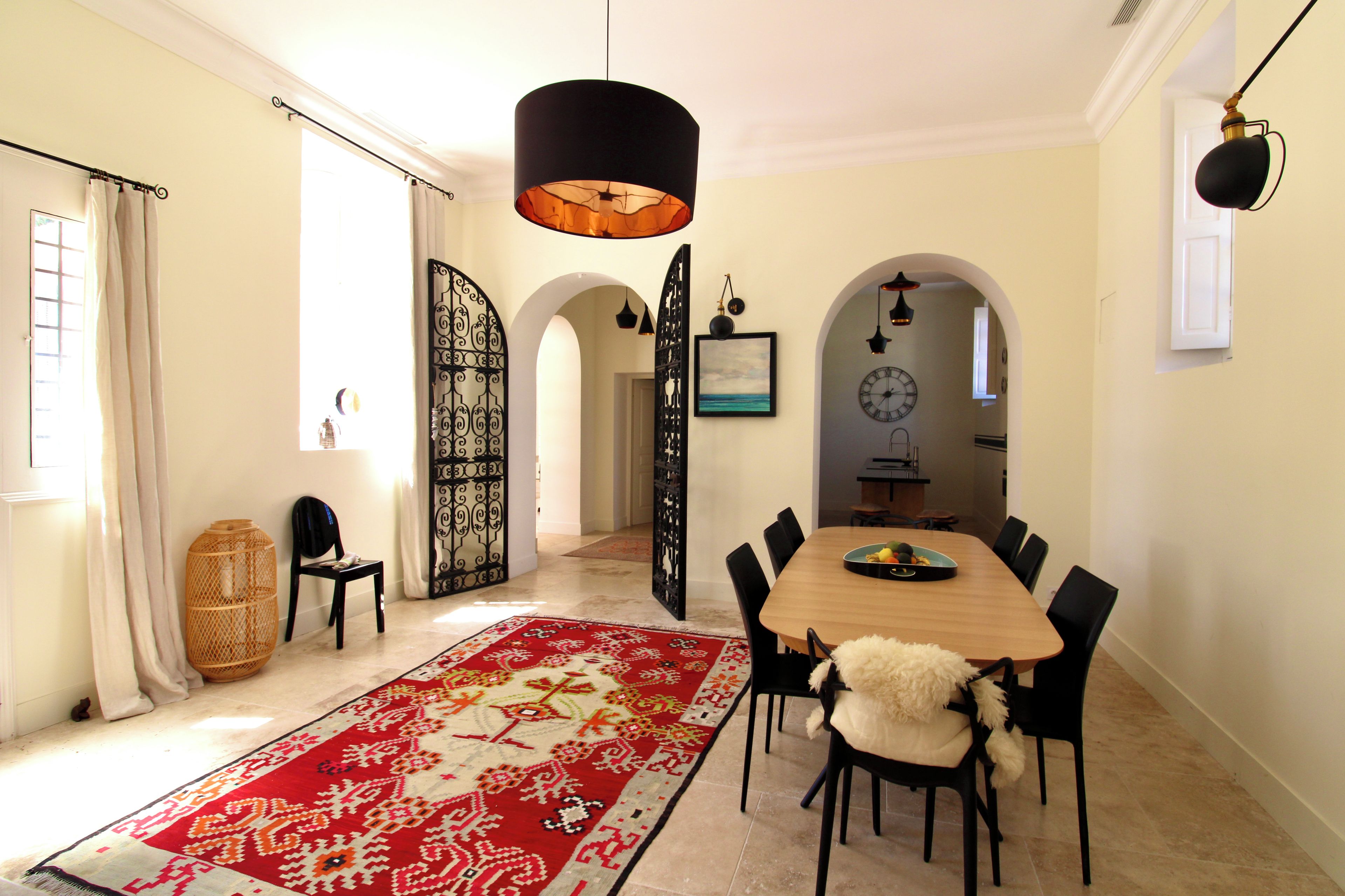 A dining area with a wooden table, black chairs, a red patterned rug, and a black pendant light.