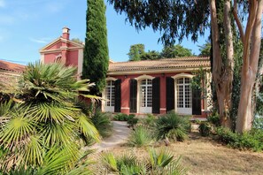 A red building with a tiled roof, a pathway leading to the entrance, and surrounding greenery. - Villa Médicis – Sleeps 10, Private Pool, A/C & Walking Distance to the Sea (Le Pradet)