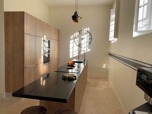 A modern kitchen with wooden cabinets, a black countertop, and a built-in oven. - Villa Médicis – Sleeps 10, Private Pool, A/C & Walking Distance to the Sea (Le Pradet)