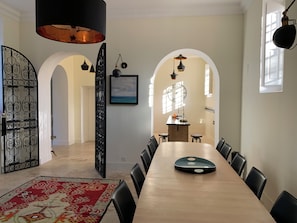 A dining area with a long table, black chairs, and a decorative rug. There are arched doorways and a kitchen area in the background. - Villa Médicis – Sleeps 10, Private Pool, A/C & Walking Distance to the Sea (Le Pradet)