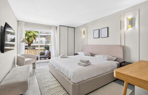 Ein modernes Hotelzimmer mit einem großen Bett, einer Sitzecke mit einem Sessel, einem kleinen Tisch und einem Balkon mit Blick.