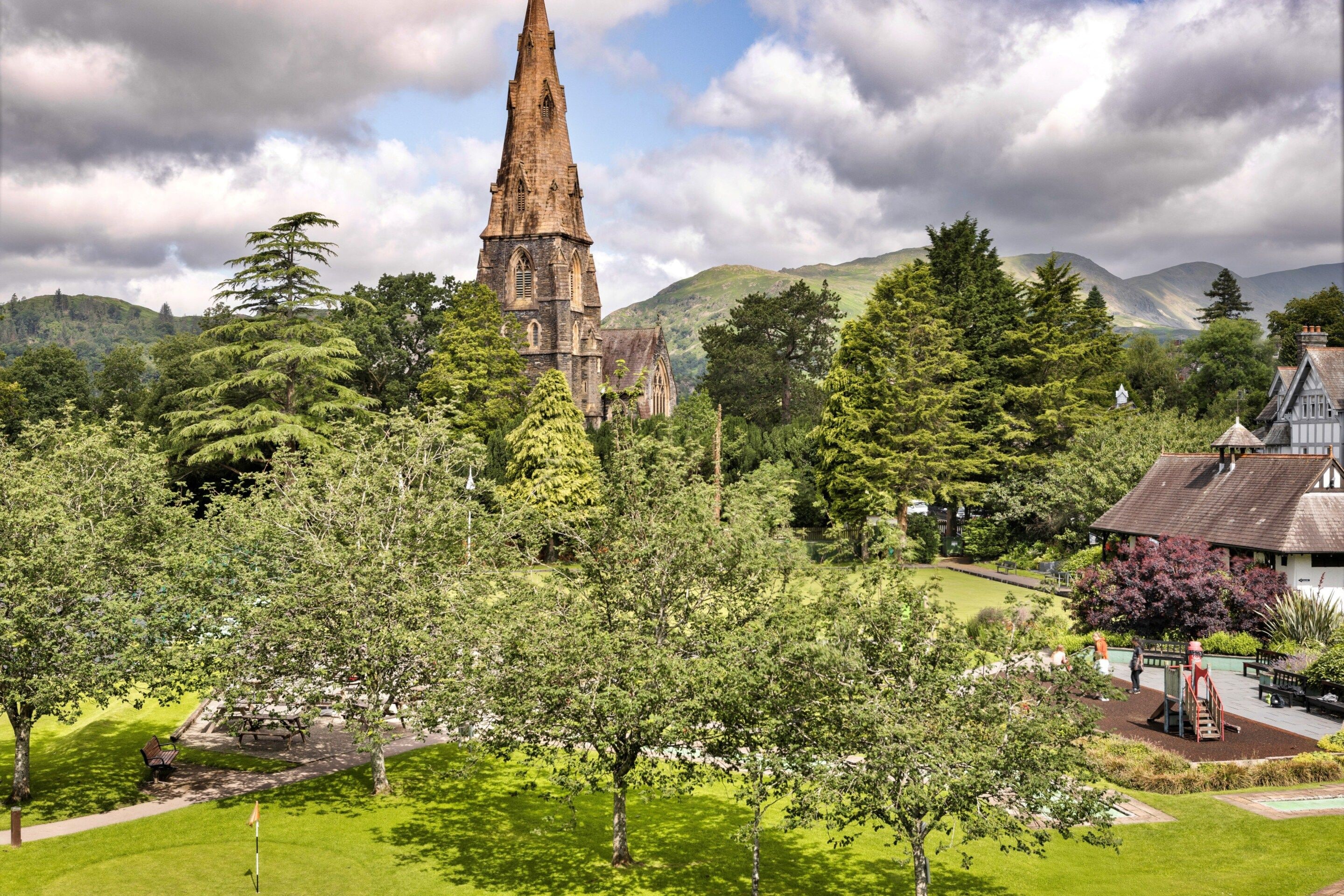 A historic church with a tall spire, surrounded by lush greenery and a small village.