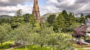 A historic church with a tall spire, surrounded by lush greenery and a small village.