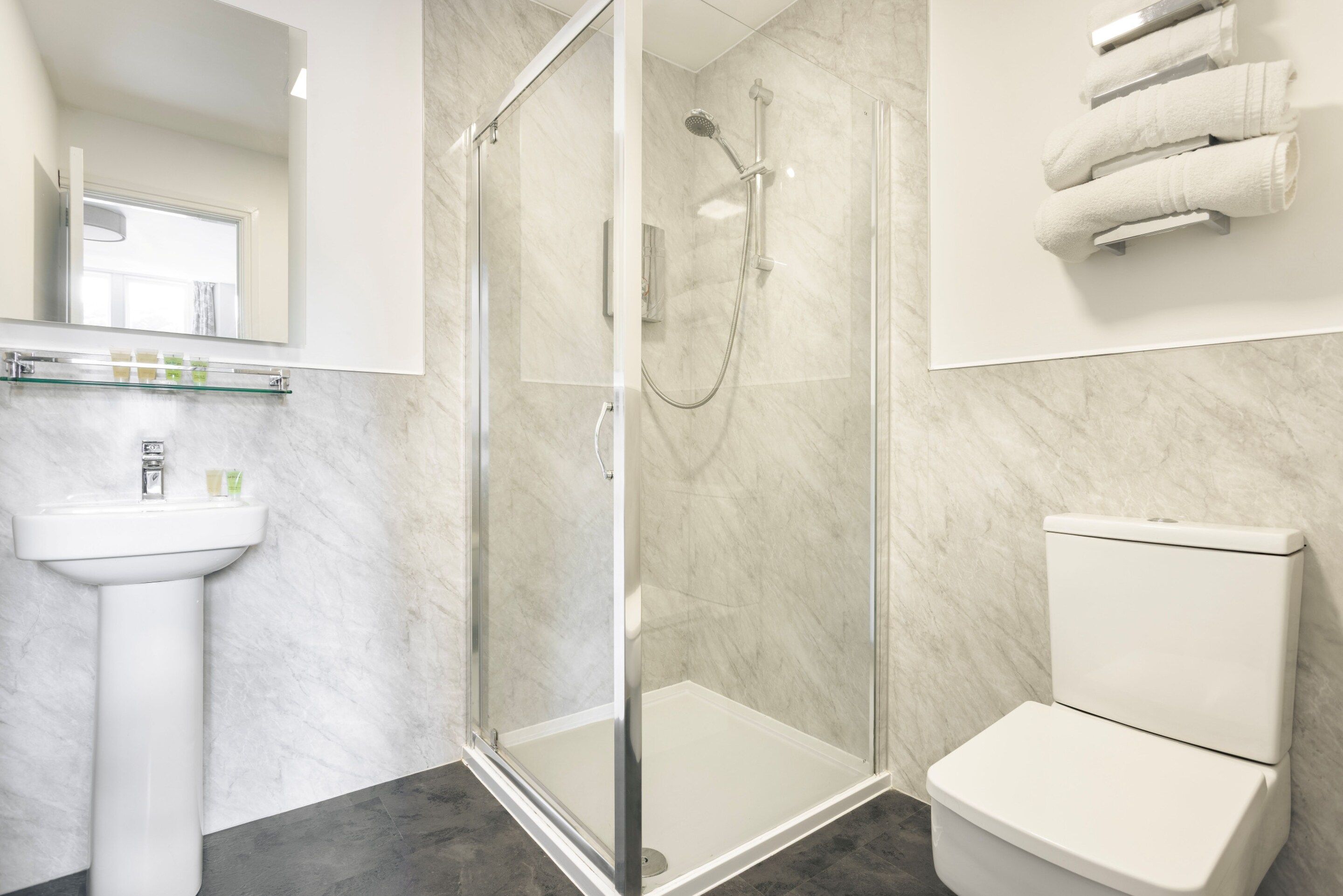 Un baño moderno con ducha envuelta en vidrio, un lavamanos blanco pedestal y un inodoro.