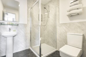 Un baño moderno con ducha envuelta en vidrio, un lavamanos blanco pedestal y un inodoro.