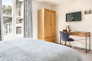 Un dormitorio con cama, un armario de madera, un escritorio con silla, un televisor en la pared y una ventana con cortinas.