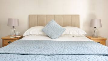 A neatly made bed with a blue quilt, two bedside lamps, a wooden nightstand, and a book.