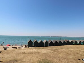 A beach with a row of beach huts, a sandy area with benches, and the sea in the background. - The Bookshop Apartment (Cowes)