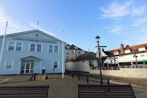 A blue building labeled 'Cowes Harbour Commission' with a traditional architectural style, a street lamp, and benches in the foreground. - The Bookshop Apartment (Cowes)