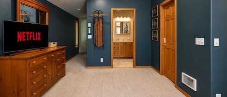 A hallway with a wooden dresser, a television displaying 'NETFLIX,' and a door leading to a bathroom.